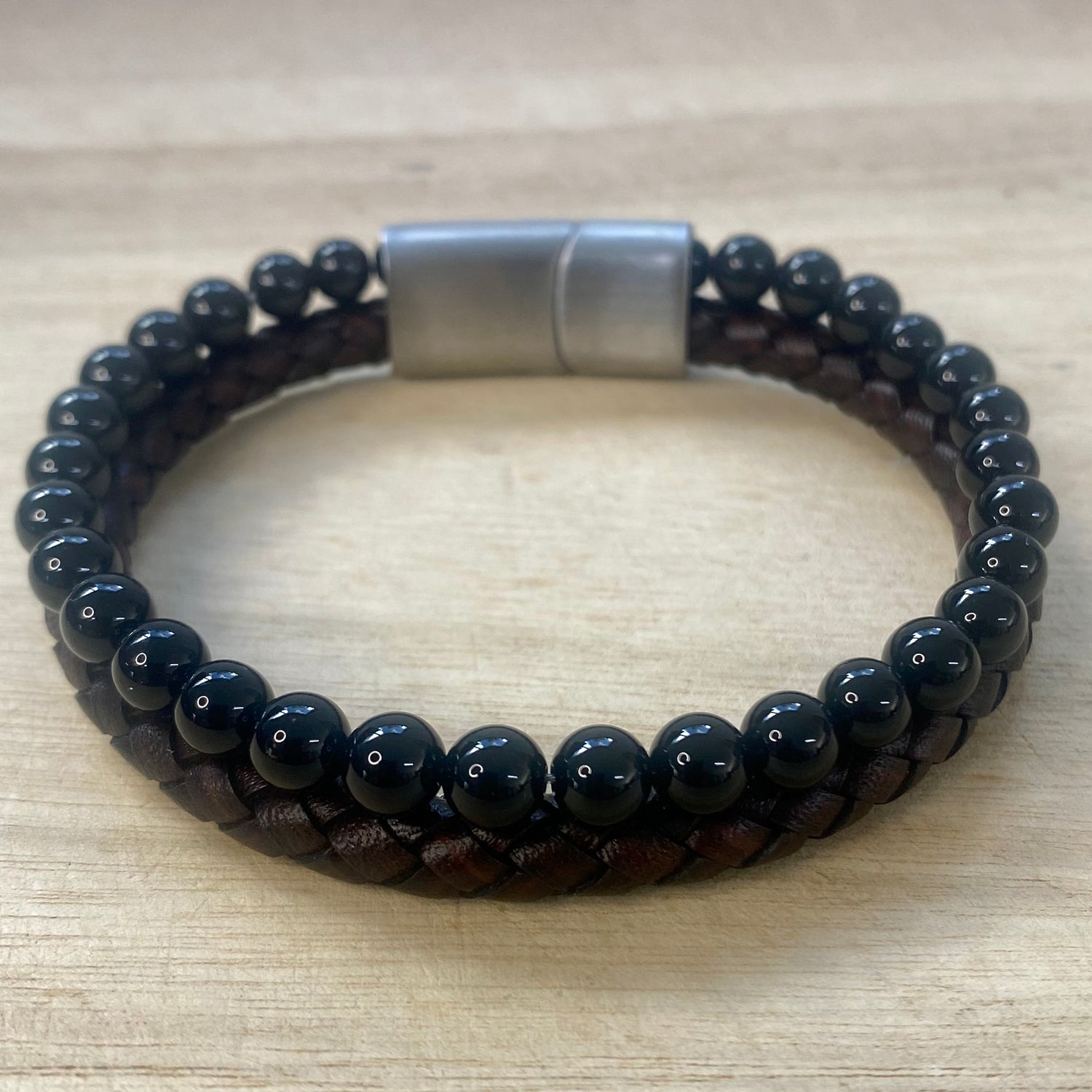 Black beaded and brown leather bracelet with a silver clasp on a wooden surface