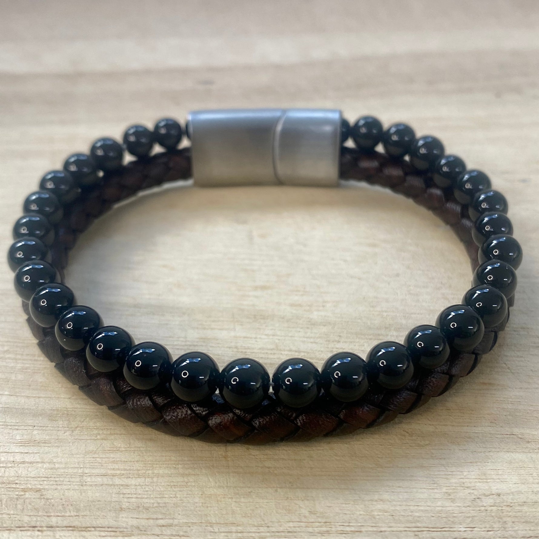 Black beaded and brown leather bracelet with a silver clasp on a wooden surface
