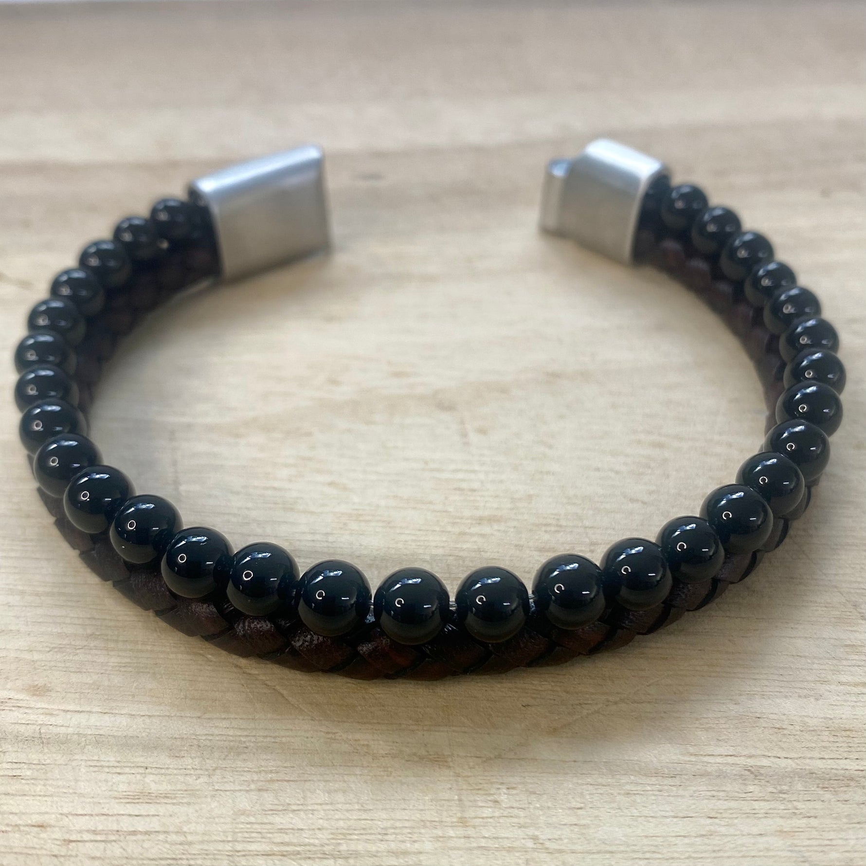 Black beaded bracelet with silver clasp on a wooden surface