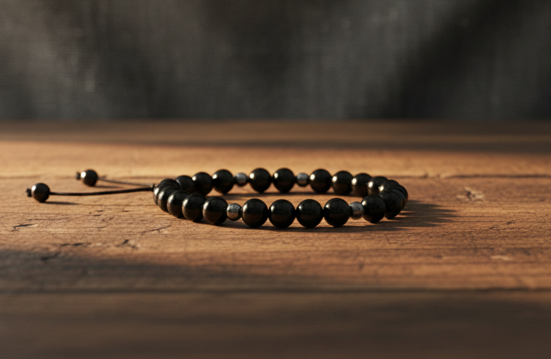 Black Obsidian and Hematite adjustable  bracelet on a wooden surface with a dark background