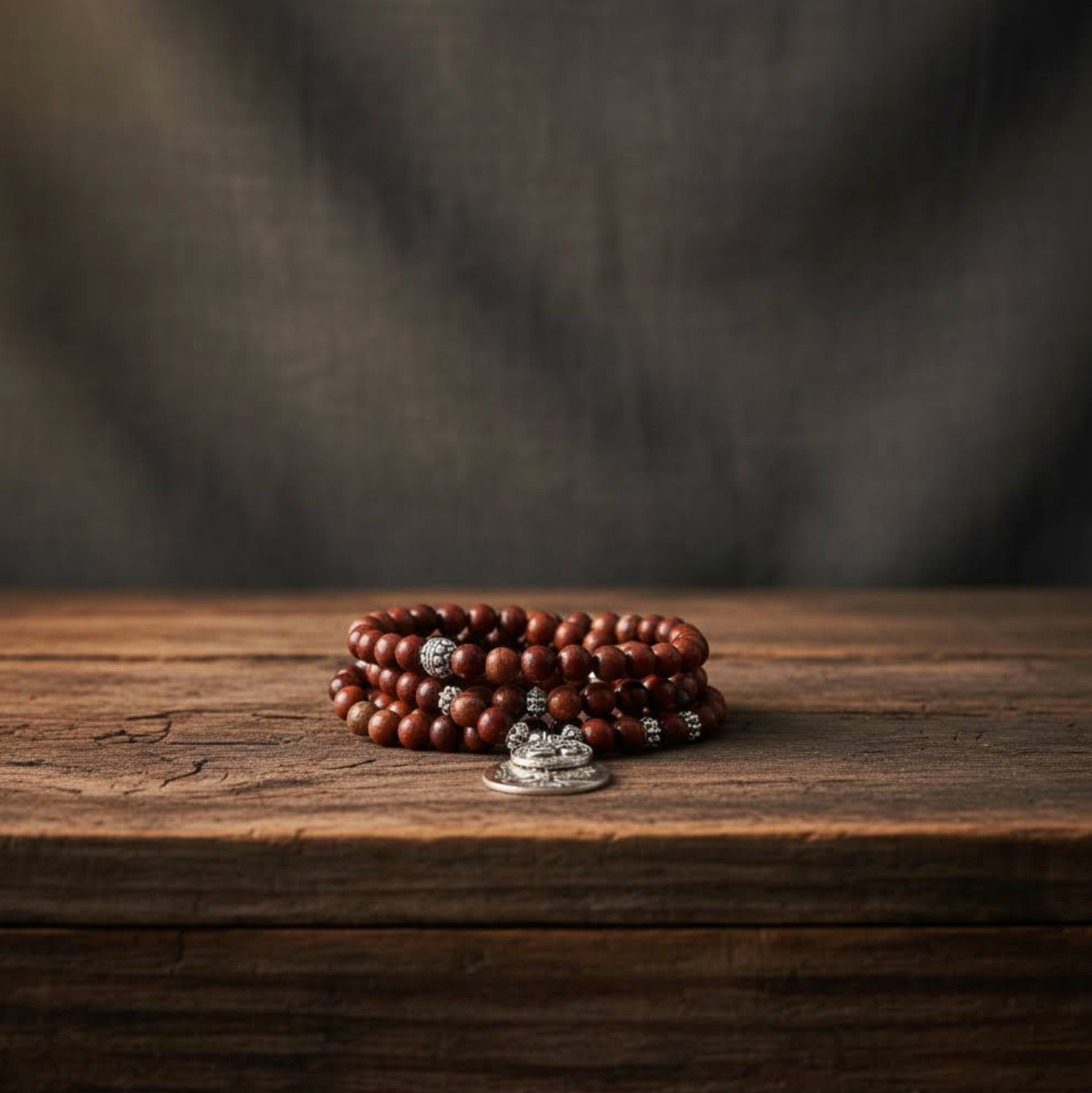 Poppy Jasper beaded bracelet with silver charms on a wooden surface